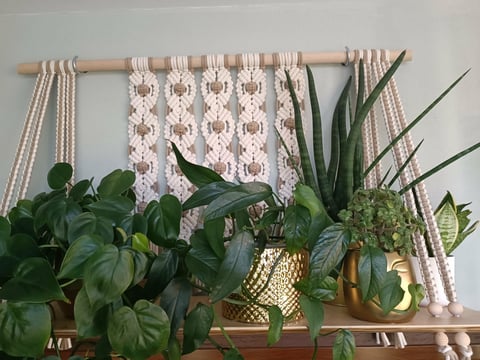 A wooden shelf displaying potted green plants with a patterned fabric hanging above on a wooden rod